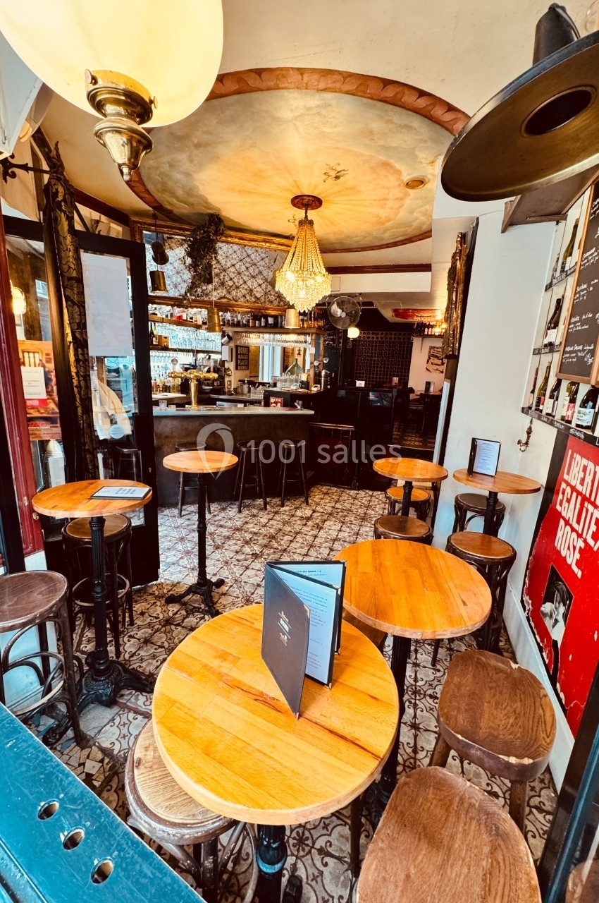 Intérieur d'un café avec tables en bois, chaises, comptoir au fond, lustre et décor mural rétro.