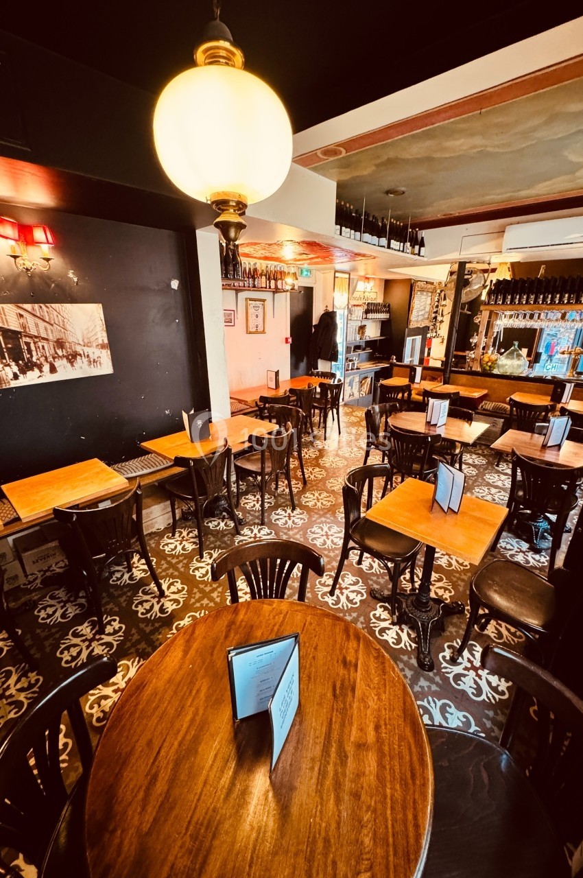 Salle de restaurant avec tables en bois, chaises noires, carrelage à motifs et éclairage chaleureux.