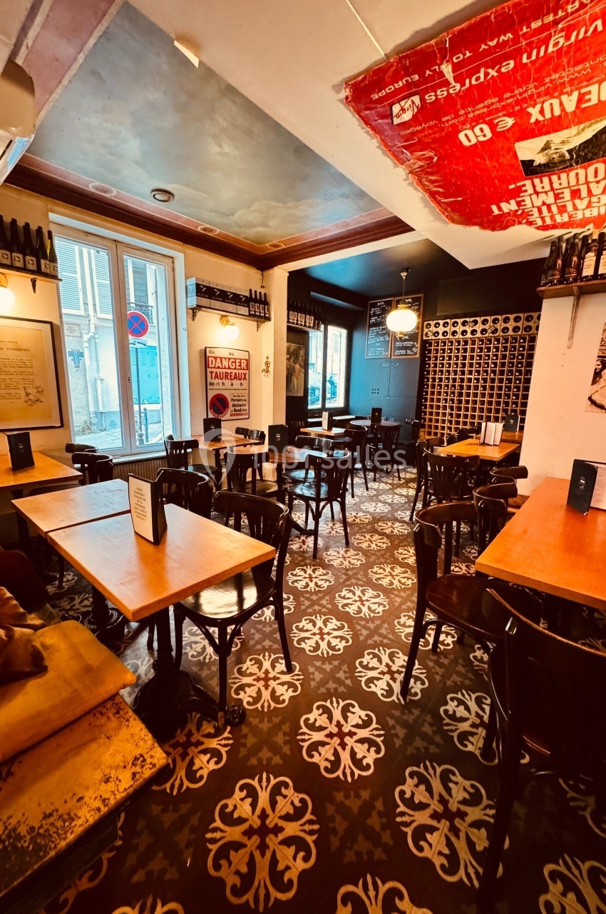 Salle de restaurant au décor vintage avec tables en bois, chaises noires et murs ornés de bouteilles de vin.
