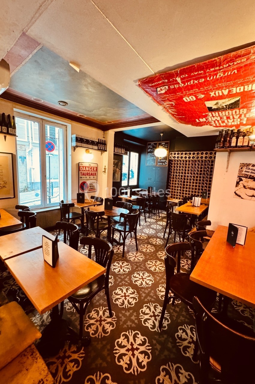 Intérieur d'un café avec tables en bois, chaises noires, décorations murales et lumière naturelle provenant d'une fenêtre.