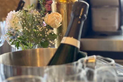 Bouteille de champagne dans un seau en métal, entourée de verres et d'un bouquet de fleurs, devant une tireuse à bière dorée.