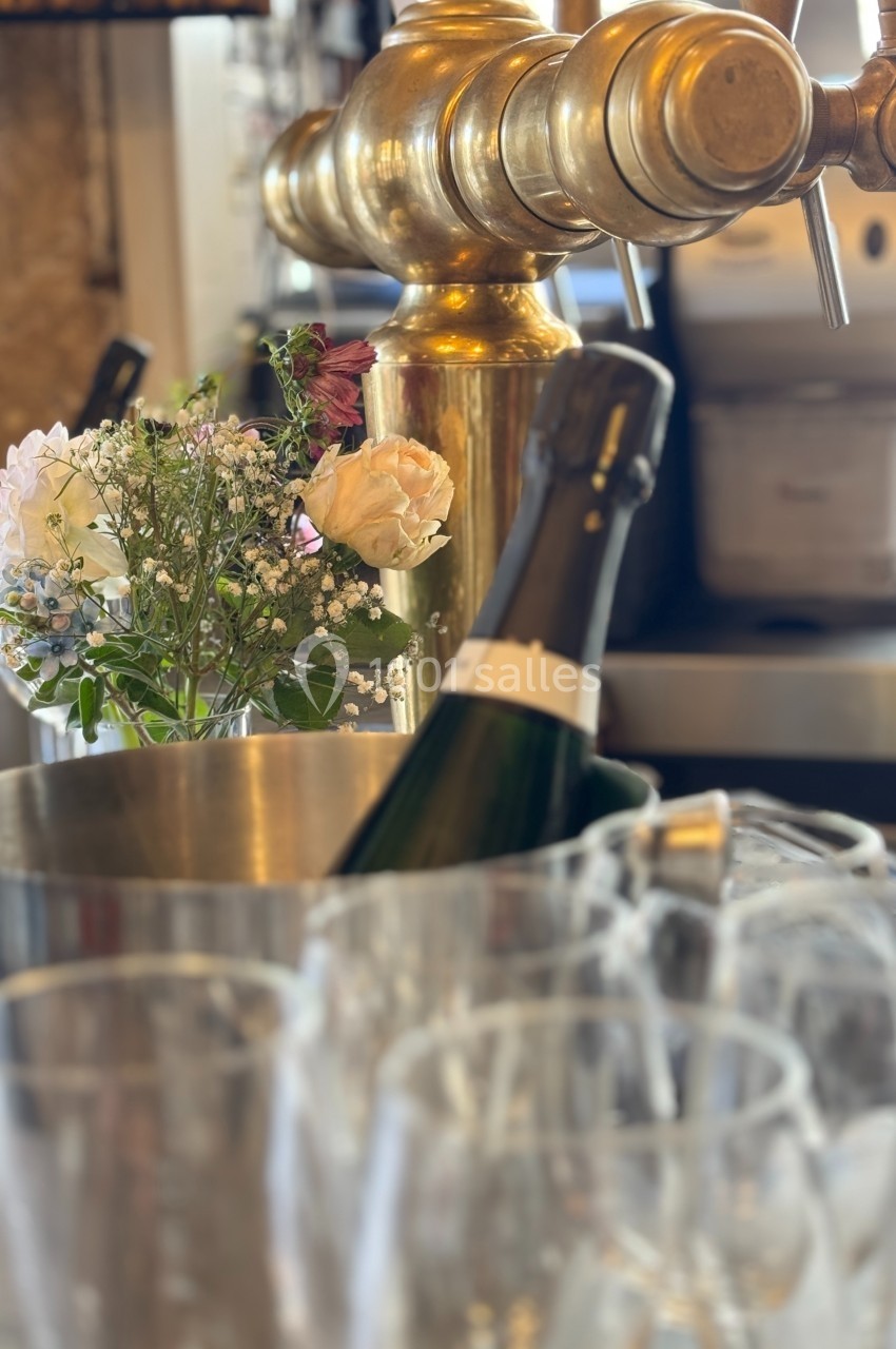 Bouteille de champagne dans un seau en métal, entourée de verres et d'un bouquet de fleurs, devant une tireuse à bière dorée.