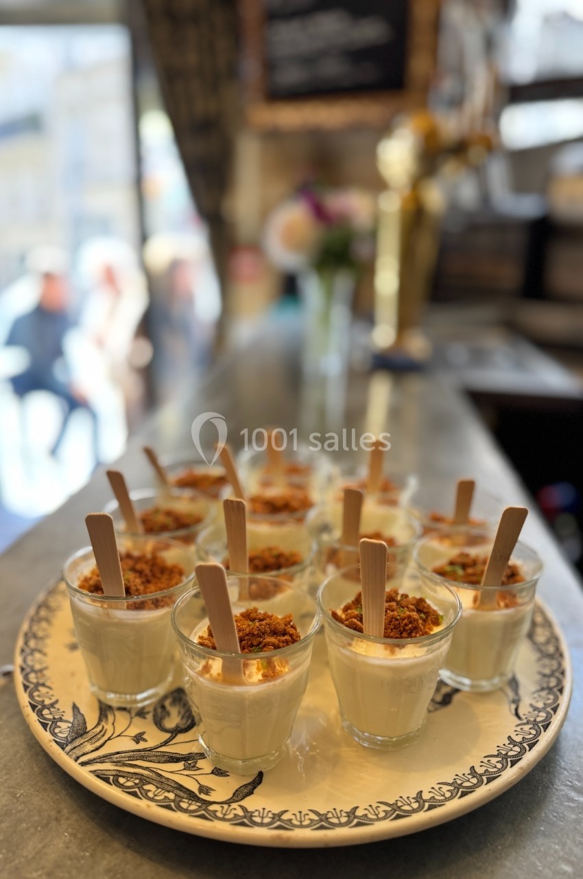 Plateau de verrines de dessert garnies de crumble et servies avec des bâtonnets en bois sur un comptoir.