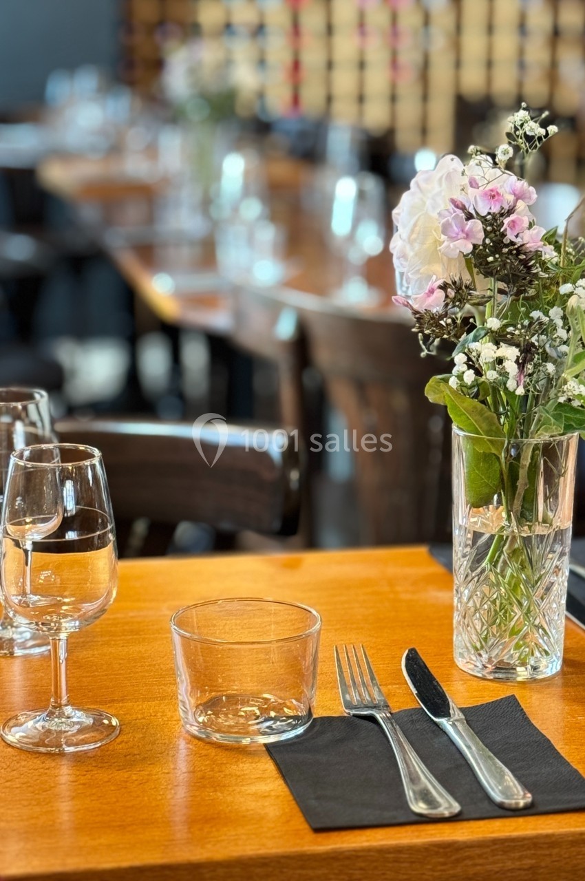 Table dressée avec des couverts, verres et un vase de fleurs, dans un restaurant à l'ambiance chaleureuse.