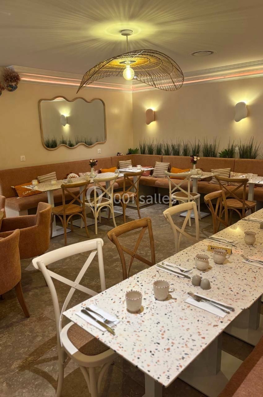 Salle de restaurant lumineuse avec tables en terrazzo, chaises en bois et banquettes décorées de coussins colorés.