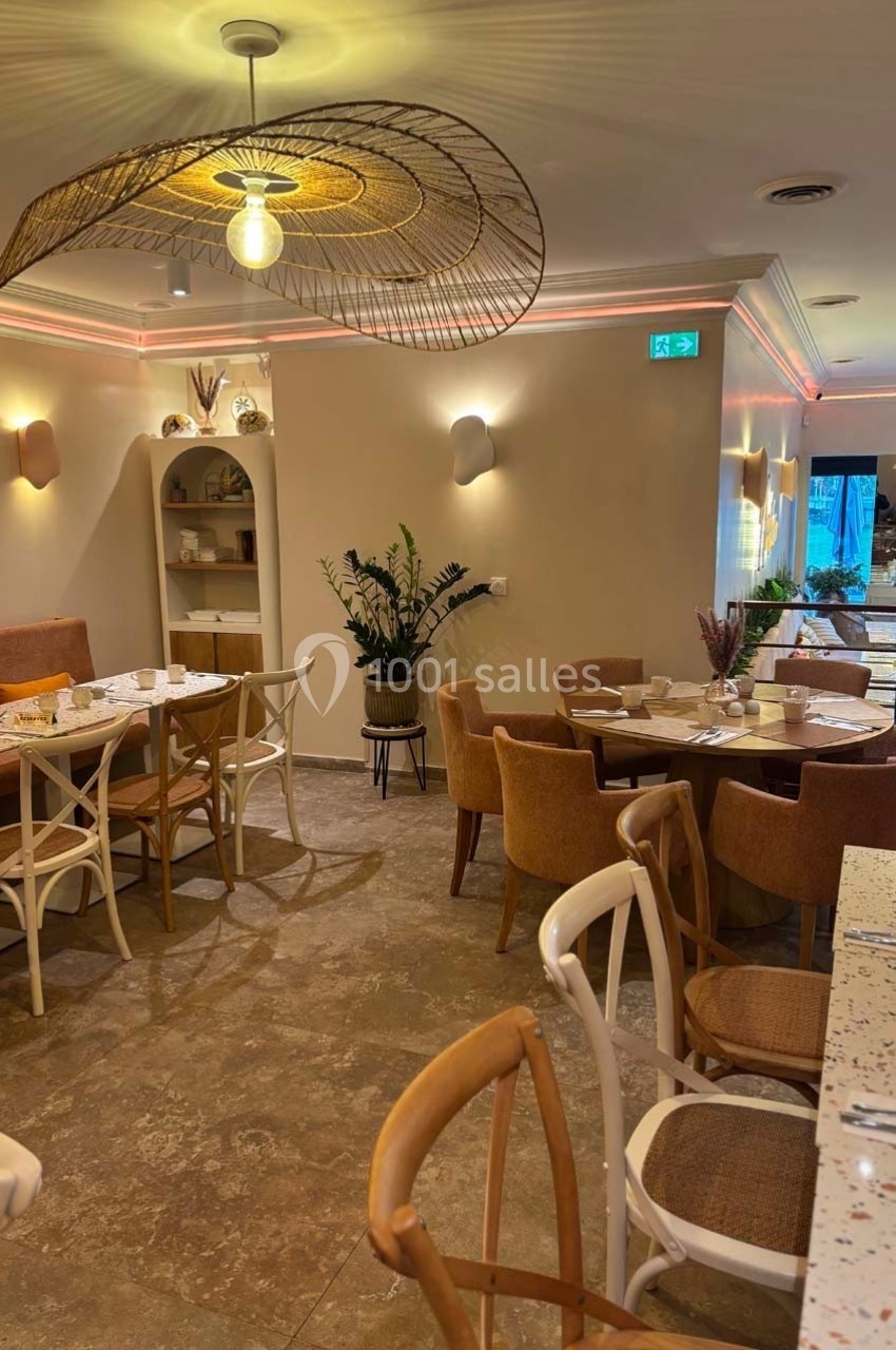 Salle de restaurant lumineuse avec mobilier en bois clair, plantes décoratives et éclairage moderne.