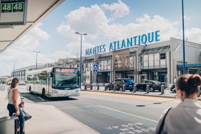 Un homme en costume charge une valise dans le coffre ouvert d'une voiture devant un bâtiment.