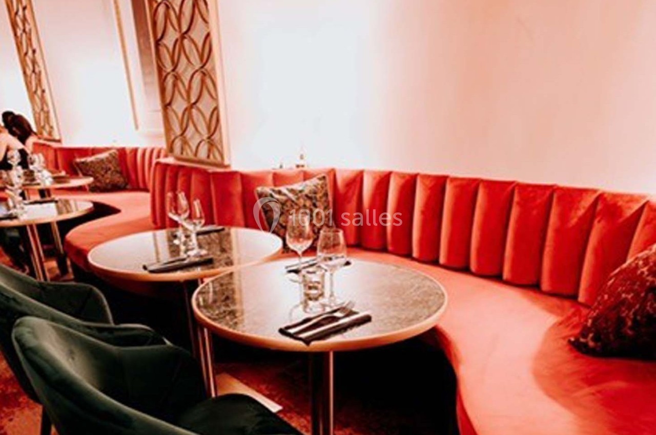 Banquettes rouges et tables rondes dressées avec verres et serviettes dans un espace intérieur chaleureux et éclairé.