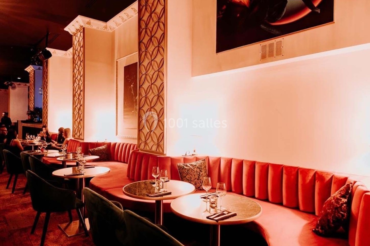Salle de restaurant élégante avec banquettes rouges, tables rondes, chaises vertes et éclairage tamisé.