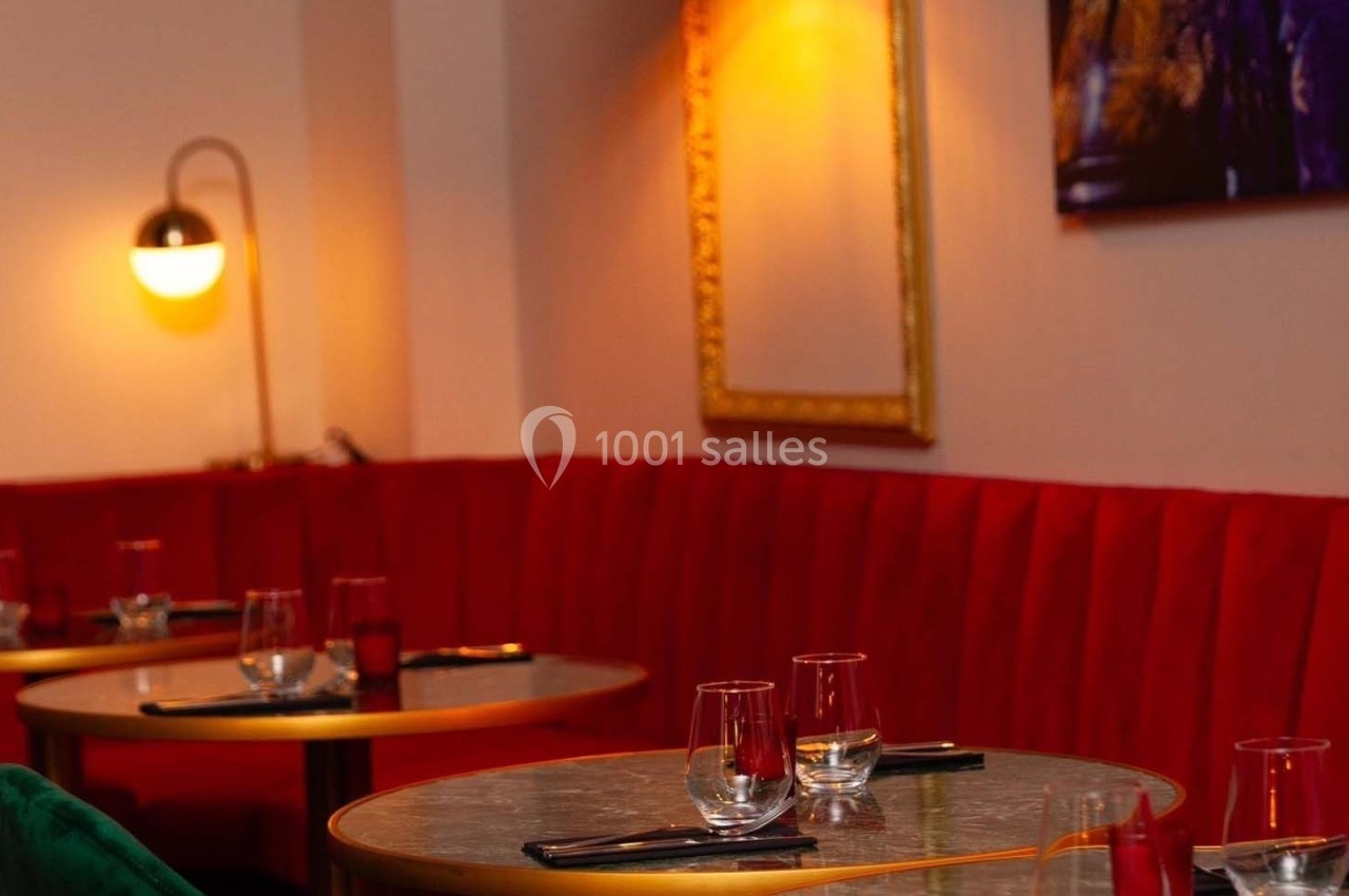 Banquettes rouges et tables rondes dressées avec verres et couverts dans un intérieur de restaurant éclairé.
