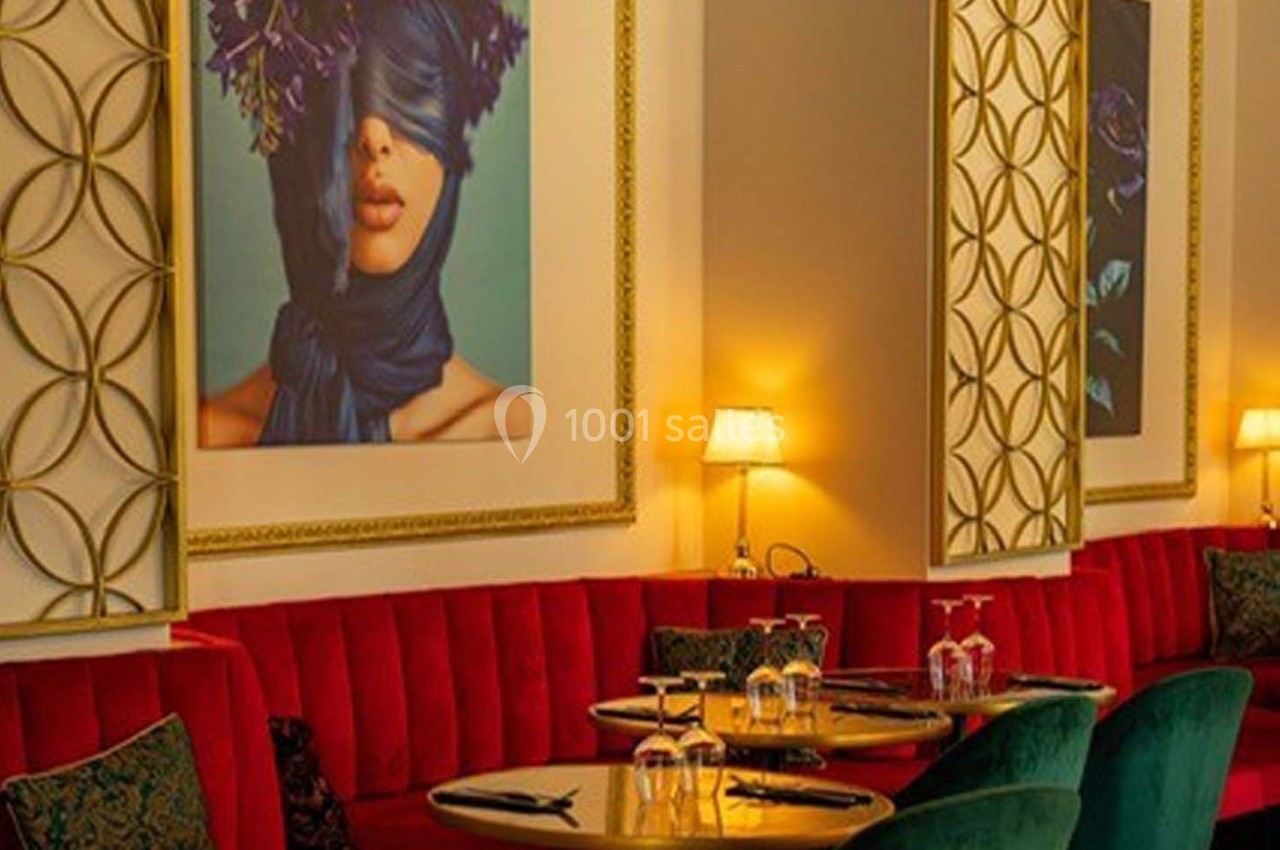 Salle de restaurant élégante avec banquettes rouges, tables dressées et tableaux artistiques sur les murs.