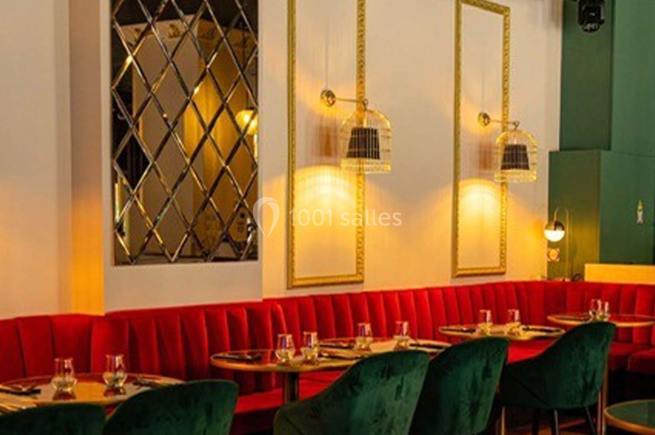 Salle de restaurant élégante avec banquettes rouges, chaises vertes, miroirs muraux et luminaires suspendus.