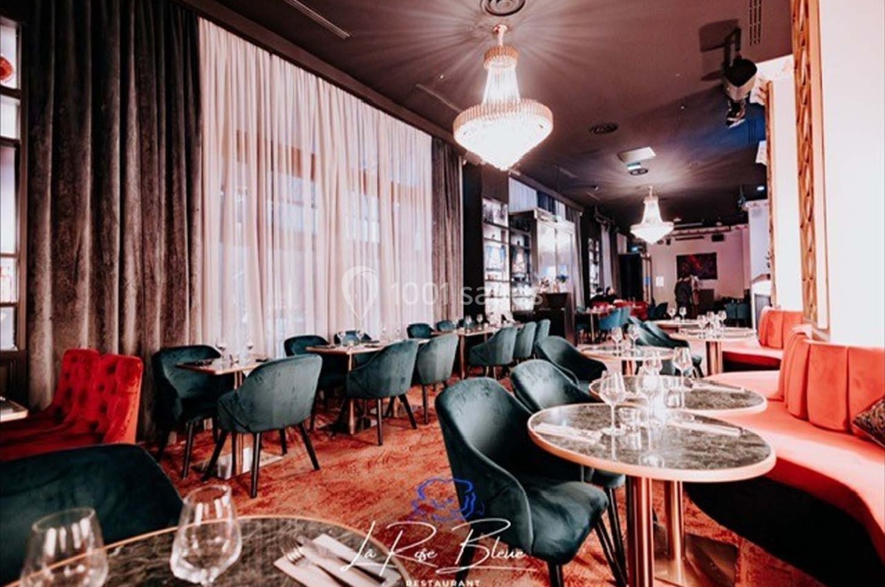 Salle de restaurant élégante avec tables dressées, chaises colorées, rideaux blancs et lustres suspendus.
