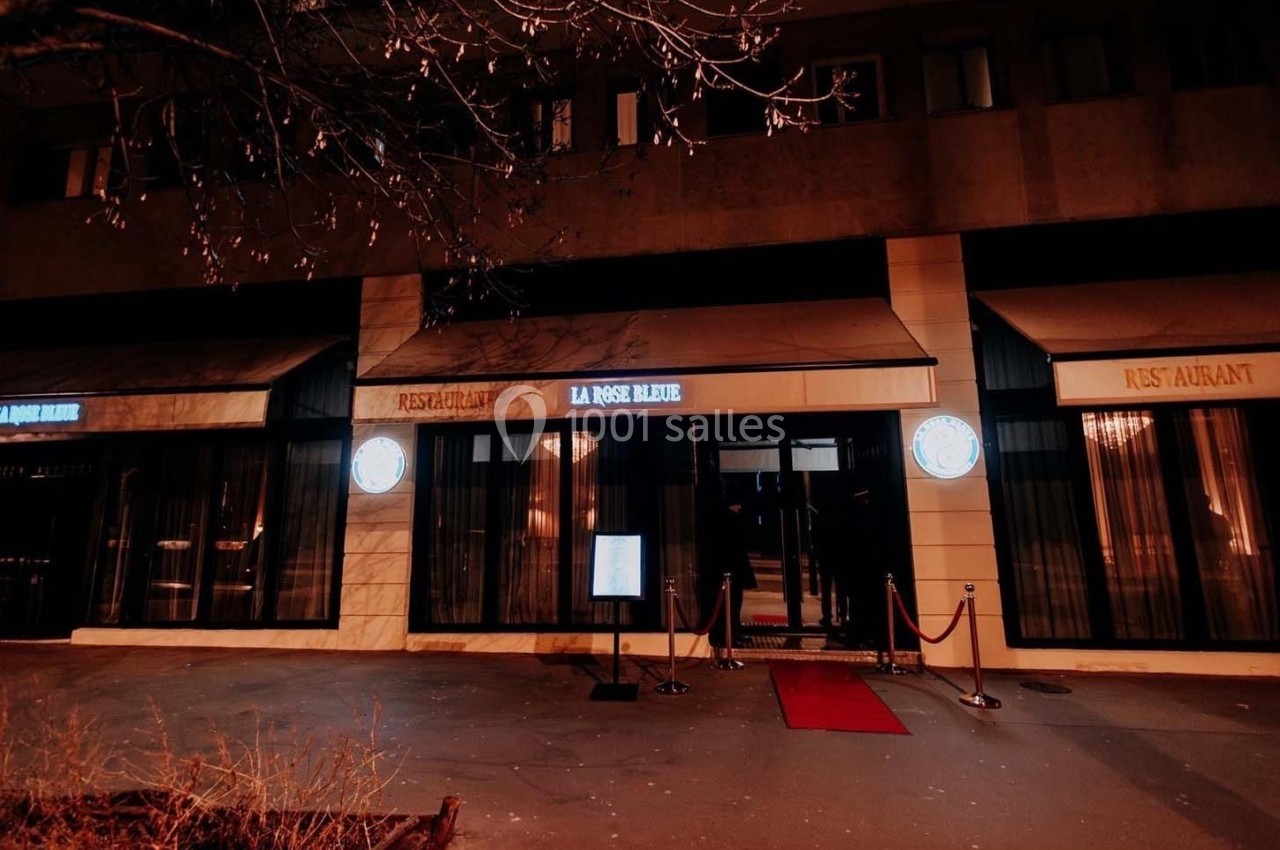 Façade d'un restaurant éclairé la nuit avec une entrée principale, un tapis rouge et des cordons de guidage.