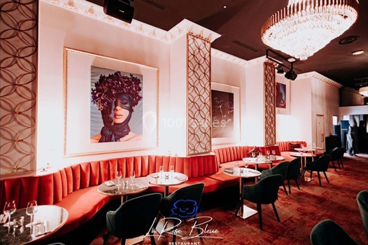 Salle de restaurant élégante avec banquettes rouges, chaises vertes, lustre imposant et œuvres d'art murales.