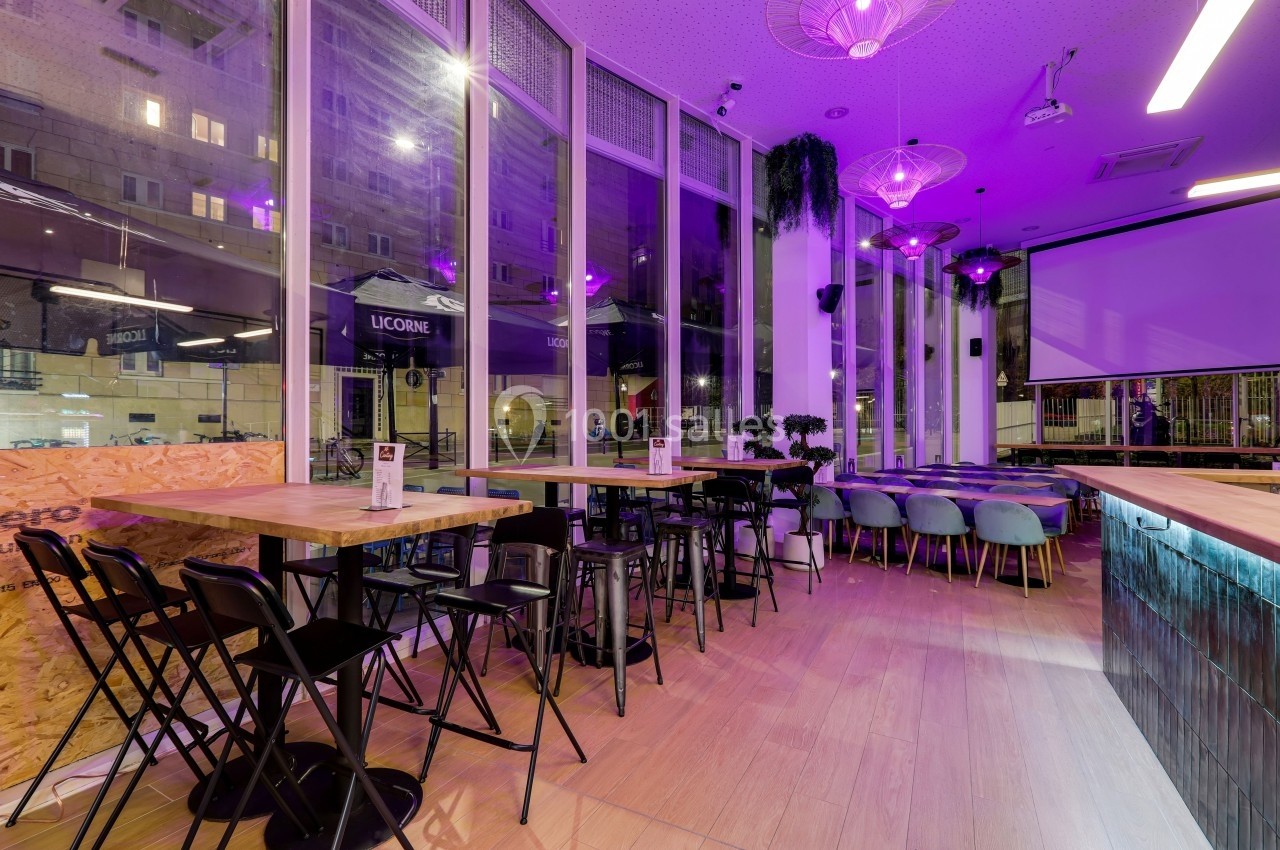 Intérieur d'un café moderne avec grandes baies vitrées, éclairage violet et mobilier en bois et métal.