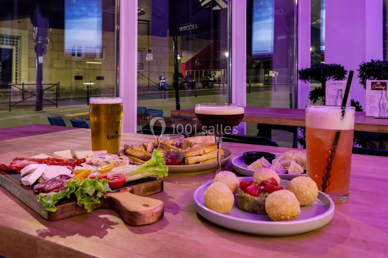 Assortiment de plats et boissons sur une table en bois dans un restaurant avec vue sur l'extérieur éclairé la nuit.