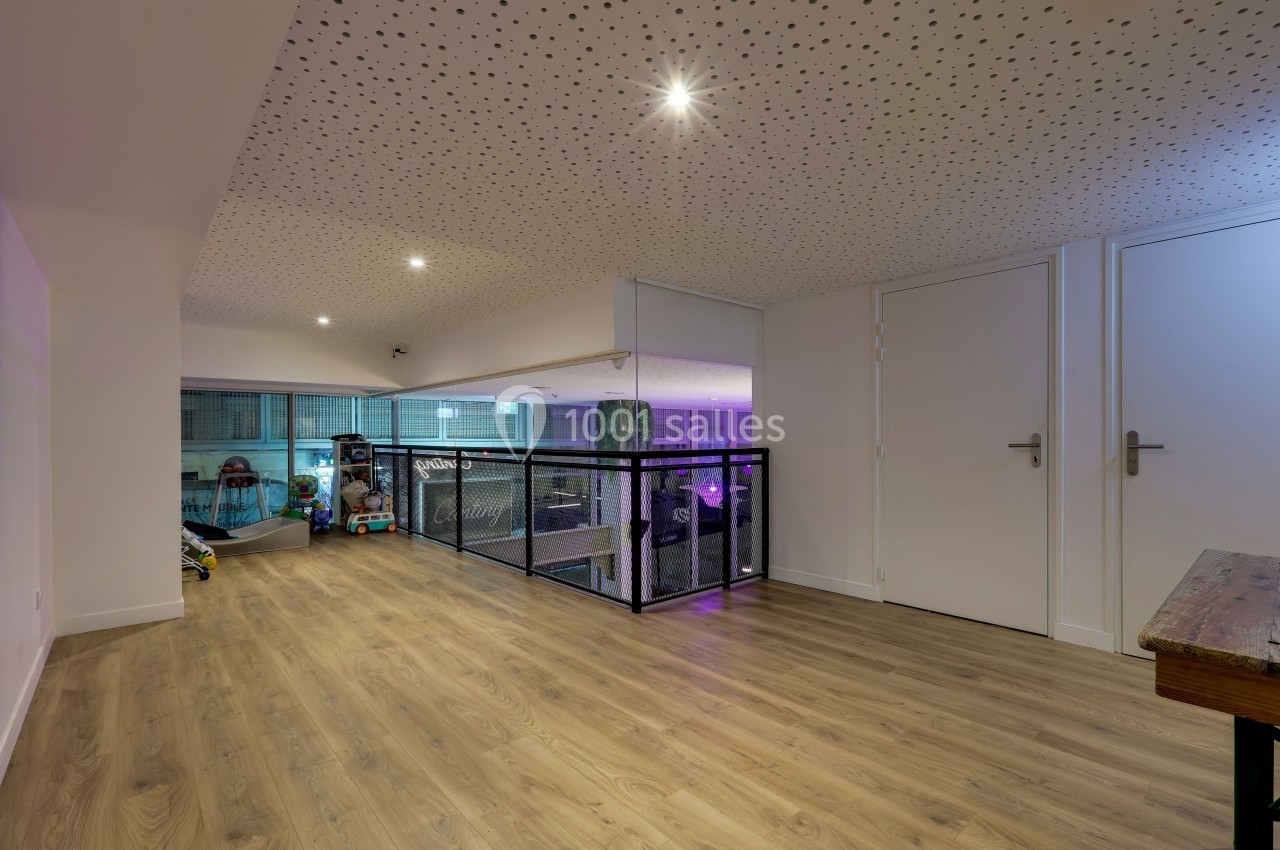 Vue d'un étage avec sol en bois, plafond perforé, garde-corps en métal et portes blanches fermées.