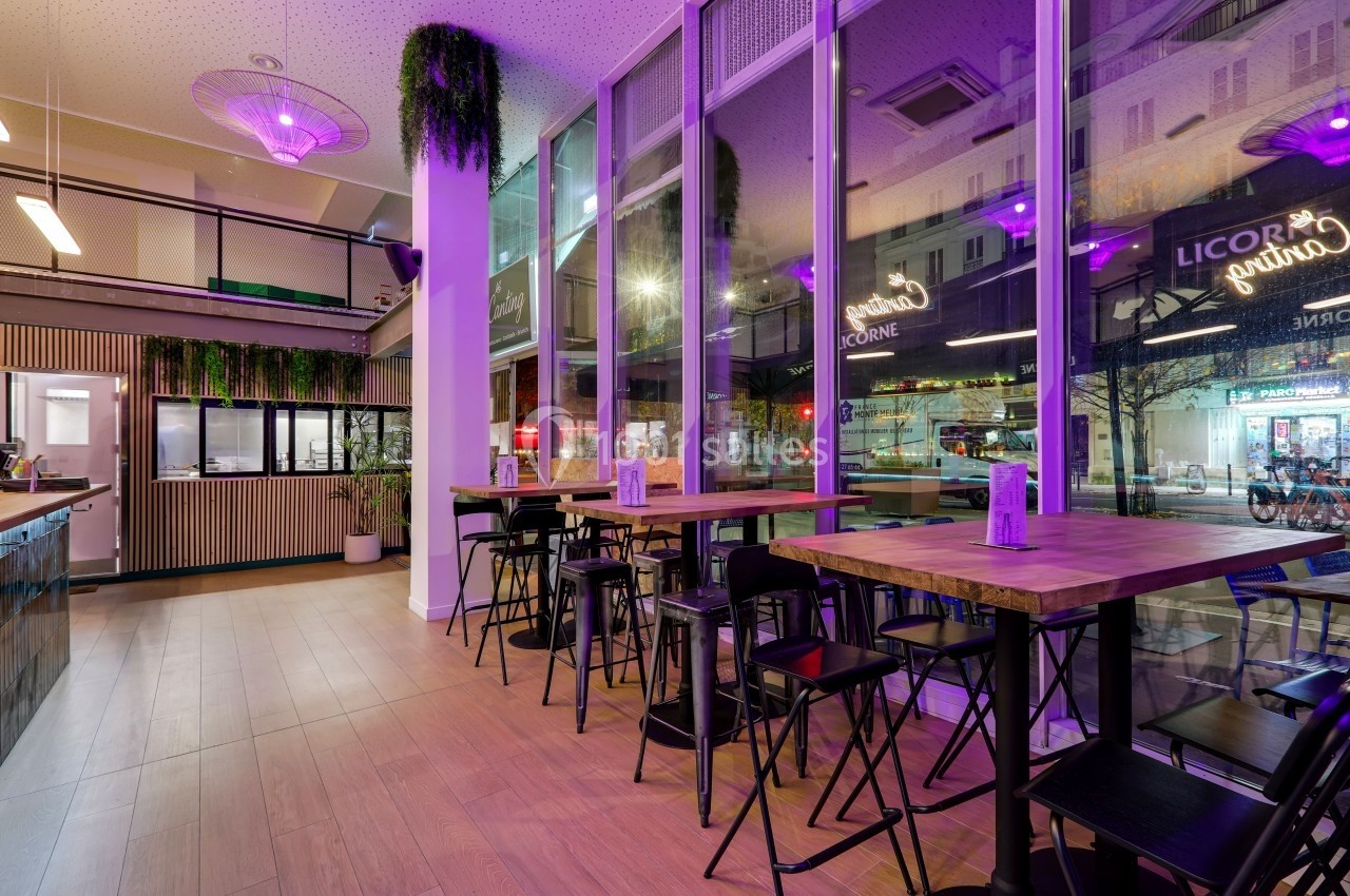 Intérieur d'un restaurant moderne avec grandes baies vitrées, éclairage violet et mobilier en bois et métal.