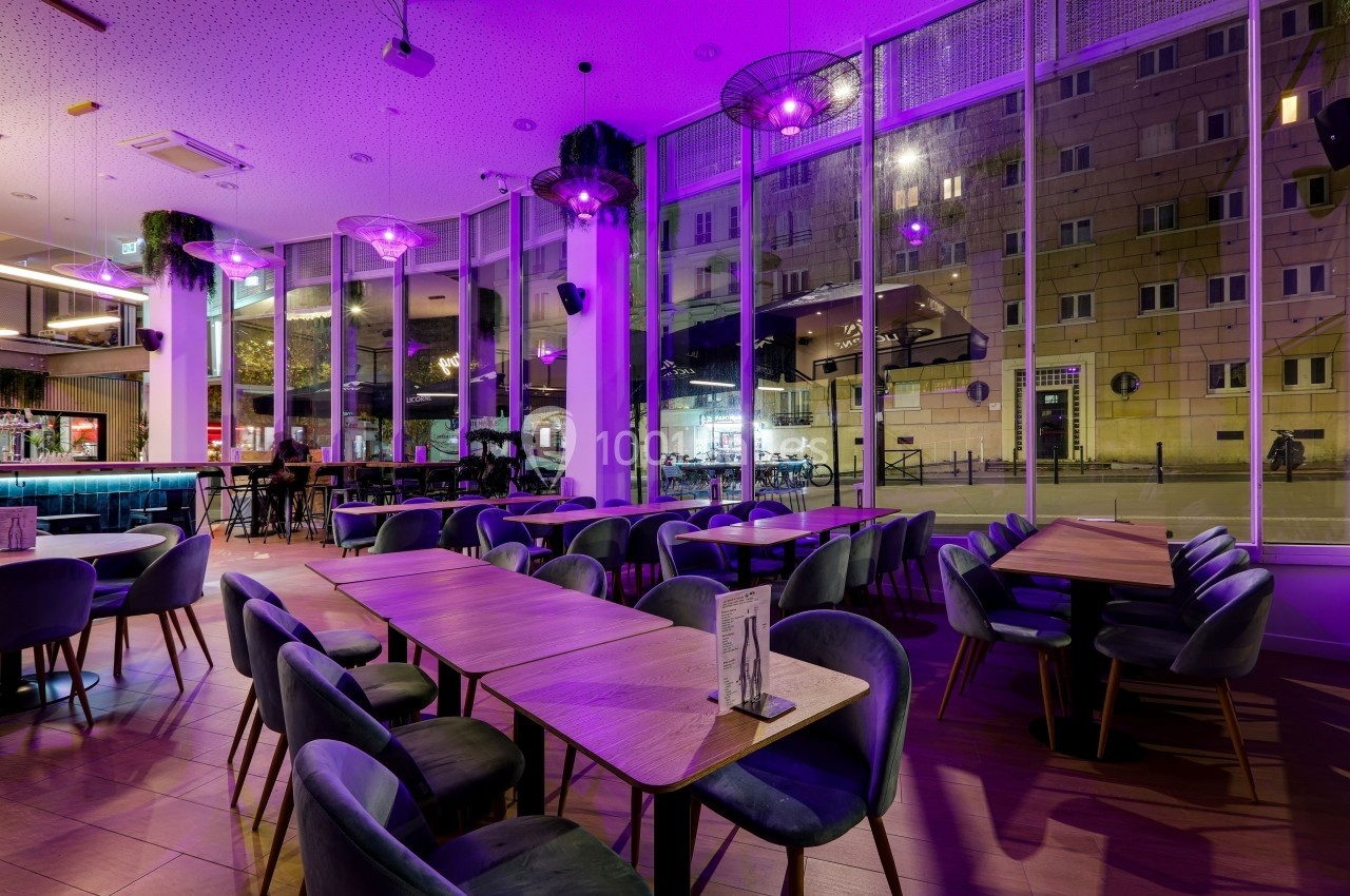 Salle de restaurant moderne avec éclairage violet, grandes baies vitrées et mobilier en bois et velours.