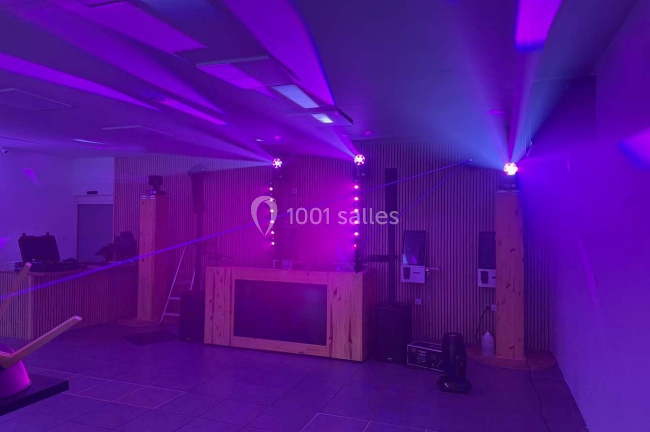 Salle avec éclairage violet, projecteurs et lasers, équipée d'une console DJ entourée de panneaux en bois.