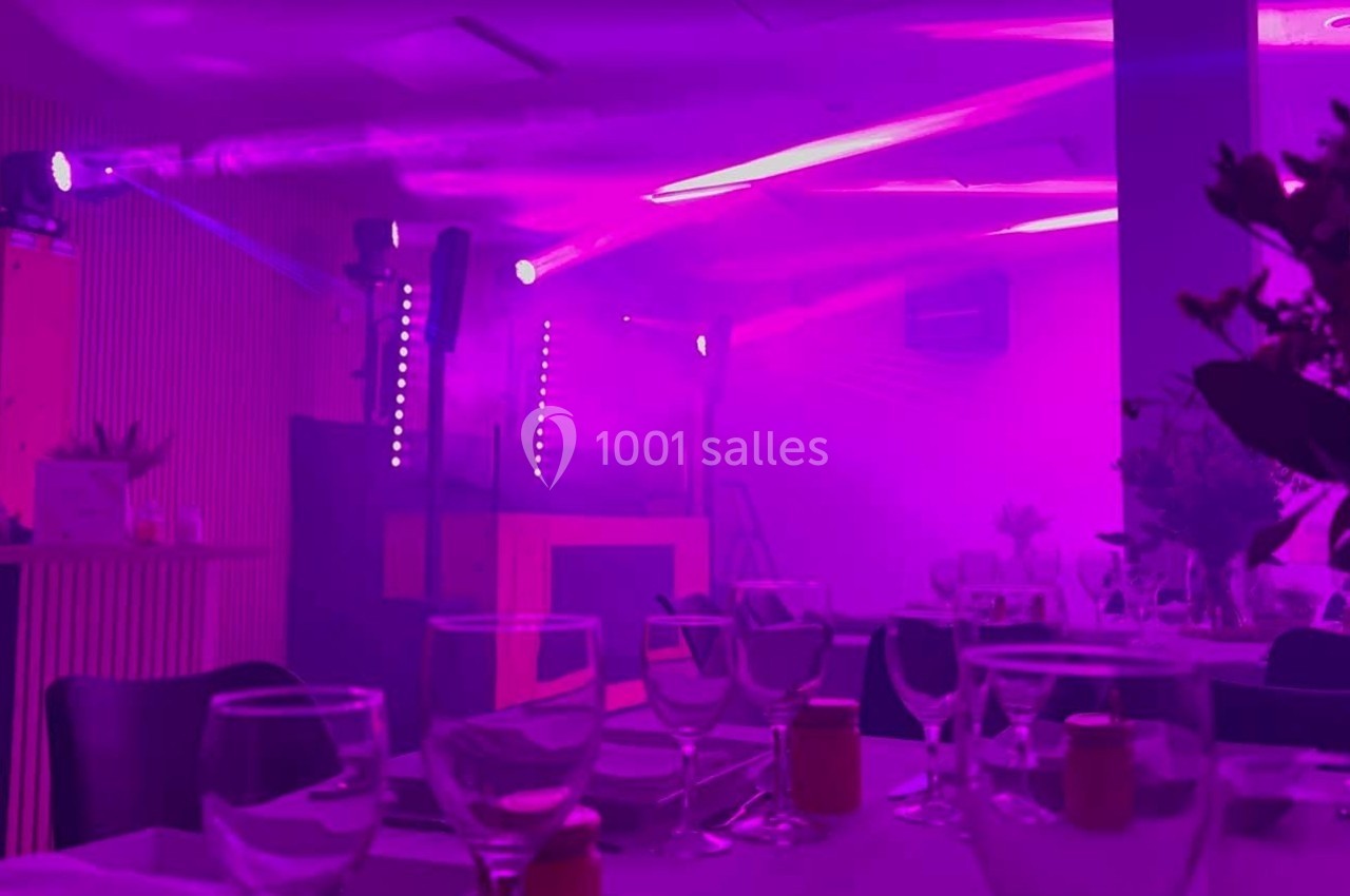 Salle de réception avec tables dressées et éclairage violet, ambiance festive avec jeux de lumière.