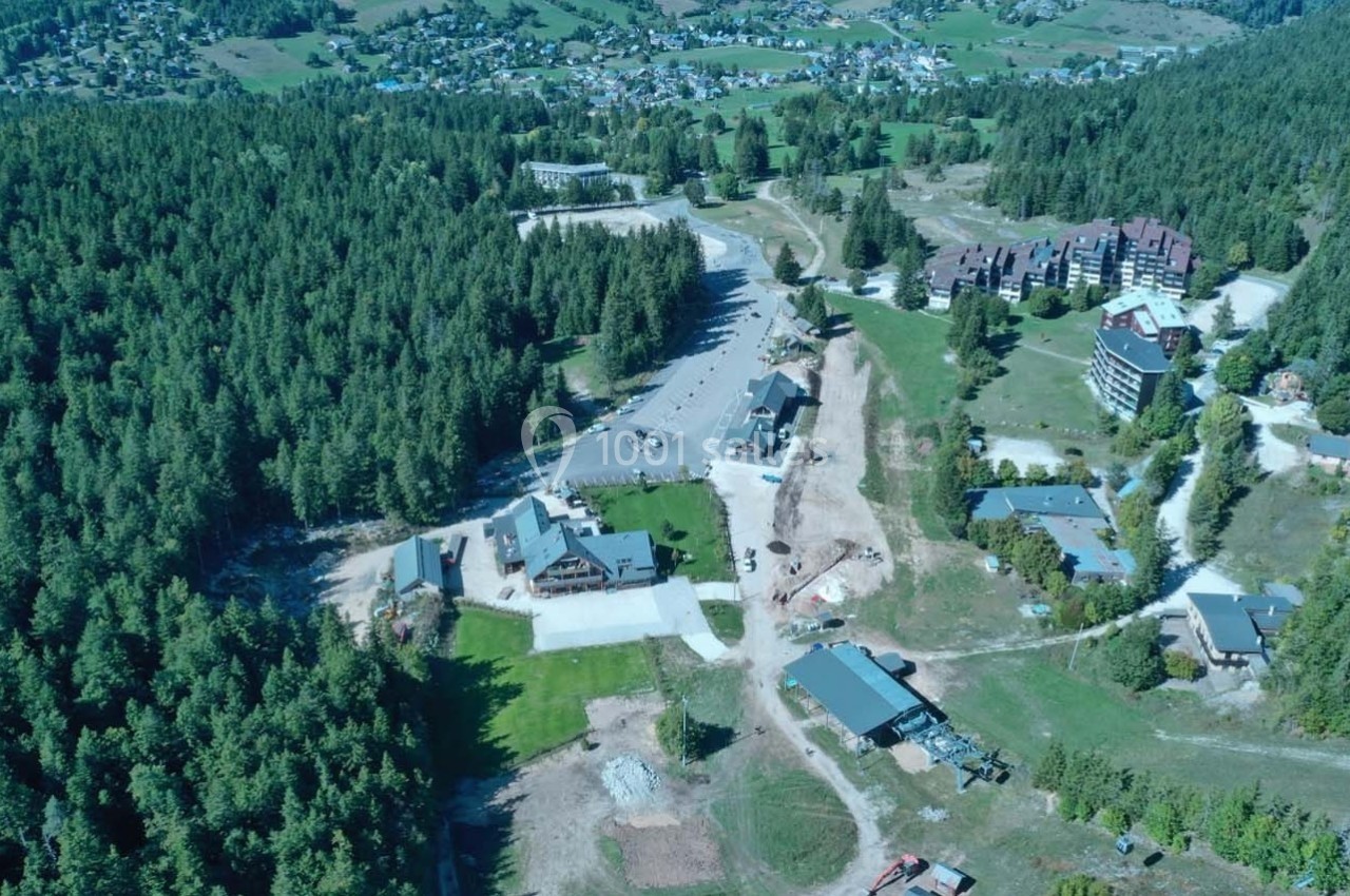 Vue aérienne d'une zone boisée avec des bâtiments dispersés, des routes et une petite ville en arrière-plan.
