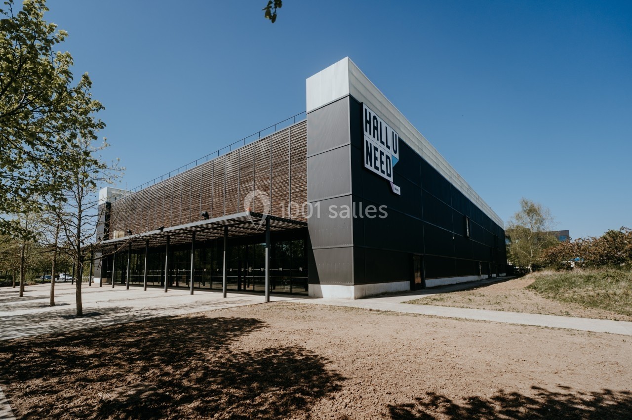 Bâtiment moderne avec façade en bois et métal, entouré d'arbres et d'un espace dégagé sous un ciel bleu.
