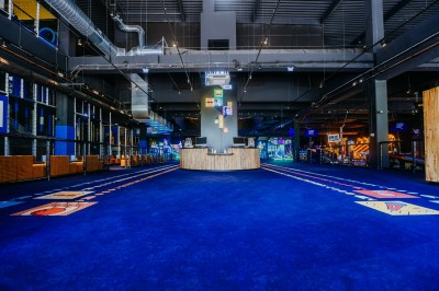 Comptoir en bois avec deux ordinateurs dans une salle d'arcade lumineuse, entourée de jeux et de machines.