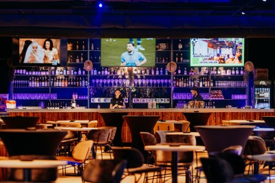 Comptoir en bois avec deux ordinateurs dans une salle d'arcade lumineuse, entourée de jeux et de machines.