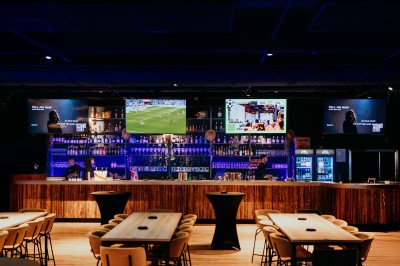 Comptoir en bois avec deux ordinateurs dans une salle d'arcade lumineuse, entourée de jeux et de machines.