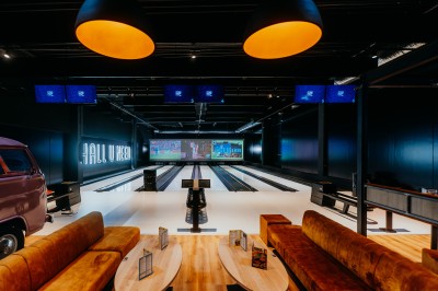 Comptoir en bois avec deux ordinateurs dans une salle d'arcade lumineuse, entourée de jeux et de machines.