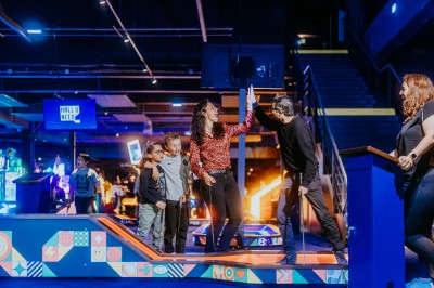 Comptoir en bois avec deux ordinateurs dans une salle d'arcade lumineuse, entourée de jeux et de machines.