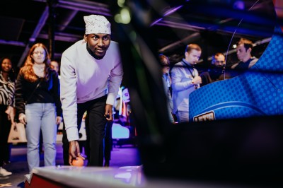 Comptoir en bois avec deux ordinateurs dans une salle d'arcade lumineuse, entourée de jeux et de machines.