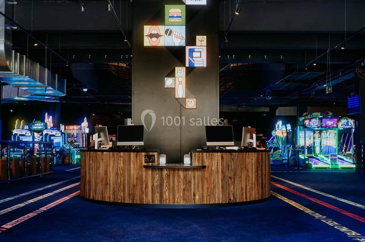 Comptoir en bois avec deux écrans dans une salle d'arcade colorée et lumineuse.