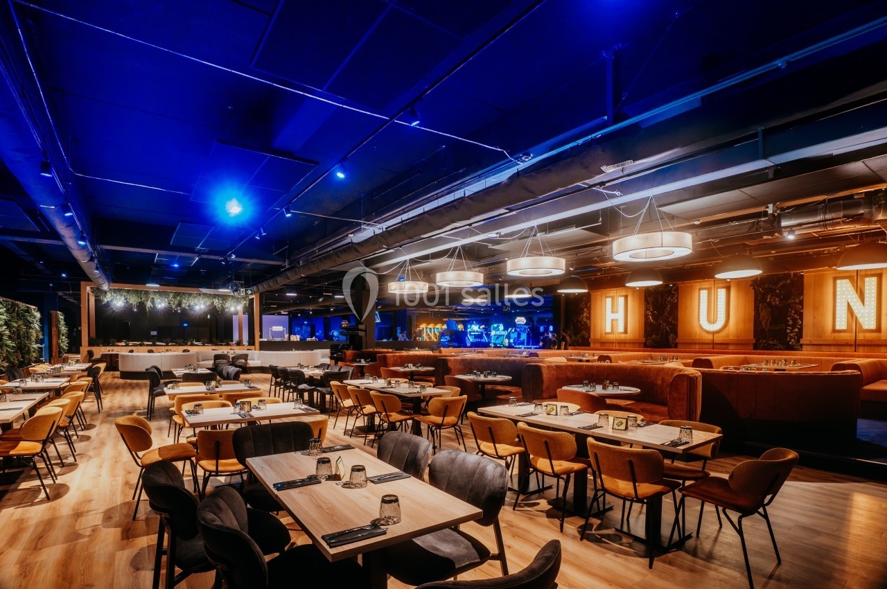 Salle de restaurant moderne avec éclairage tamisé, tables en bois, chaises rembourrées et décorations lumineuses.
