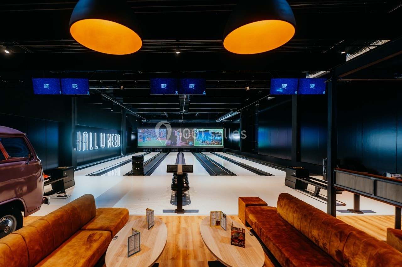 Salle de bowling moderne avec pistes alignées, écrans suspendus et espaces de détente avec canapés et tables.