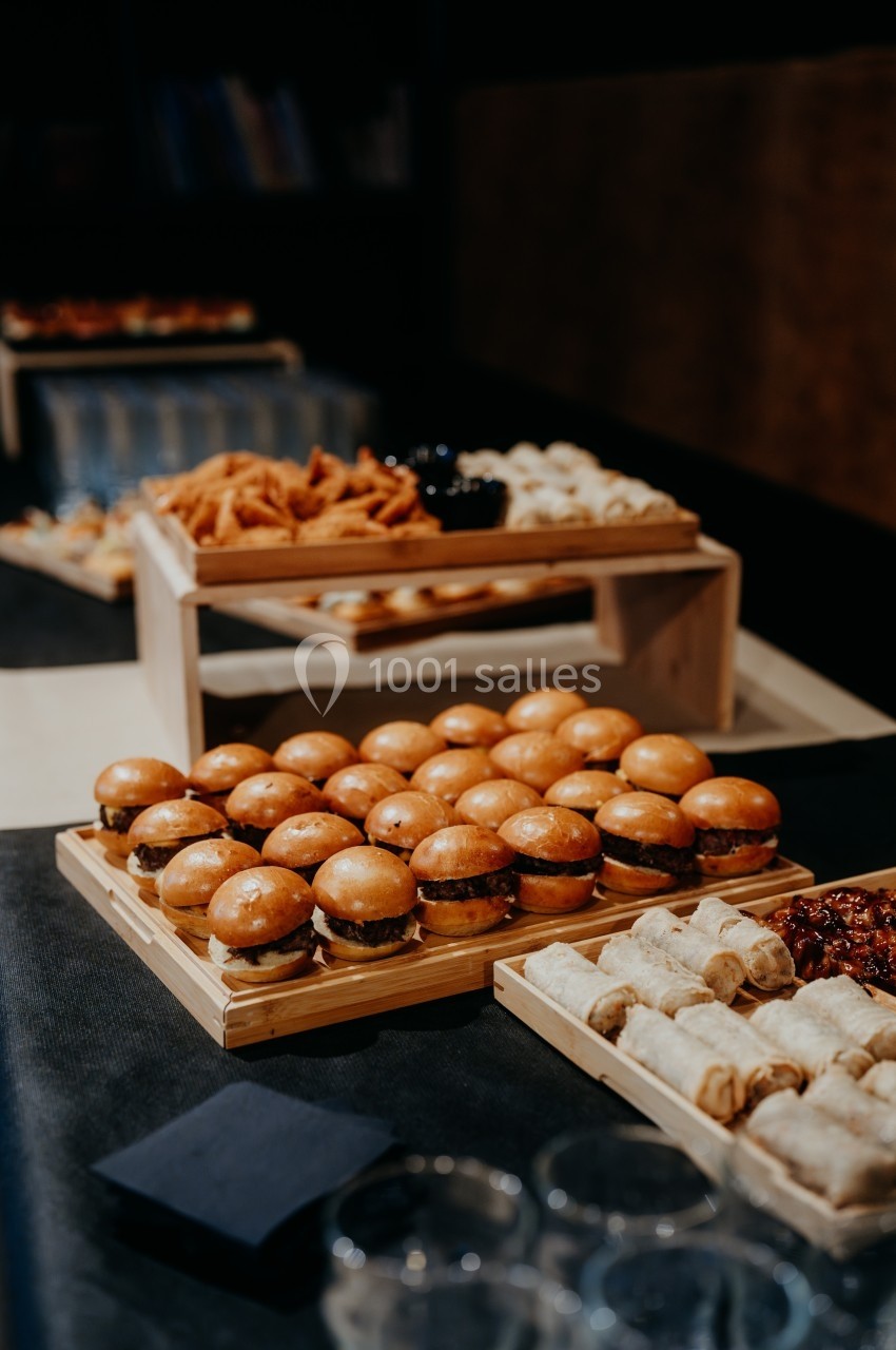 Plateau de mini-burgers, rouleaux de printemps et amuse-bouches disposés sur une table lors d’un buffet.
