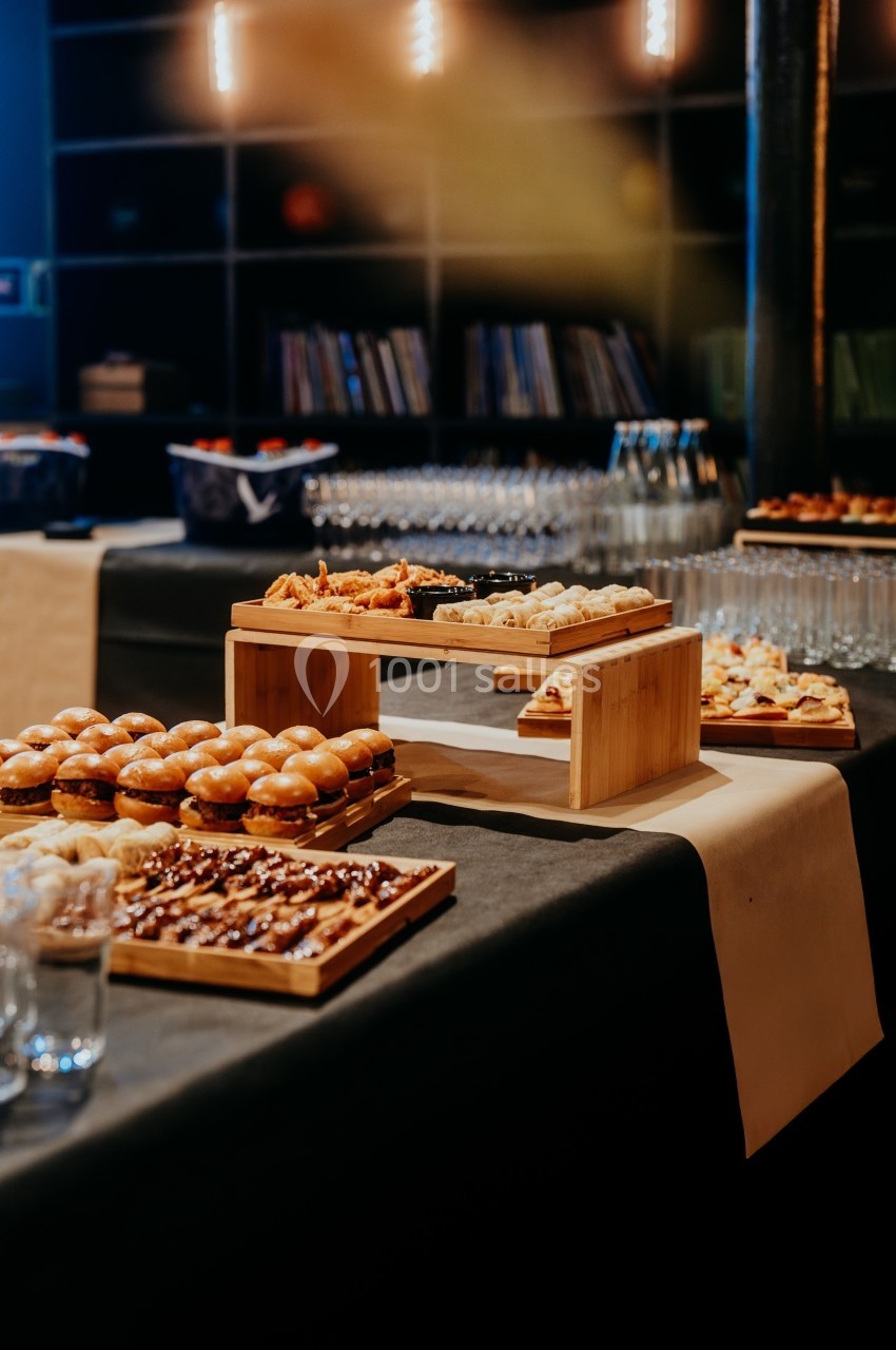Buffet avec divers plats, dont mini-sandwichs, desserts et amuse-bouches, disposés sur une table noire.