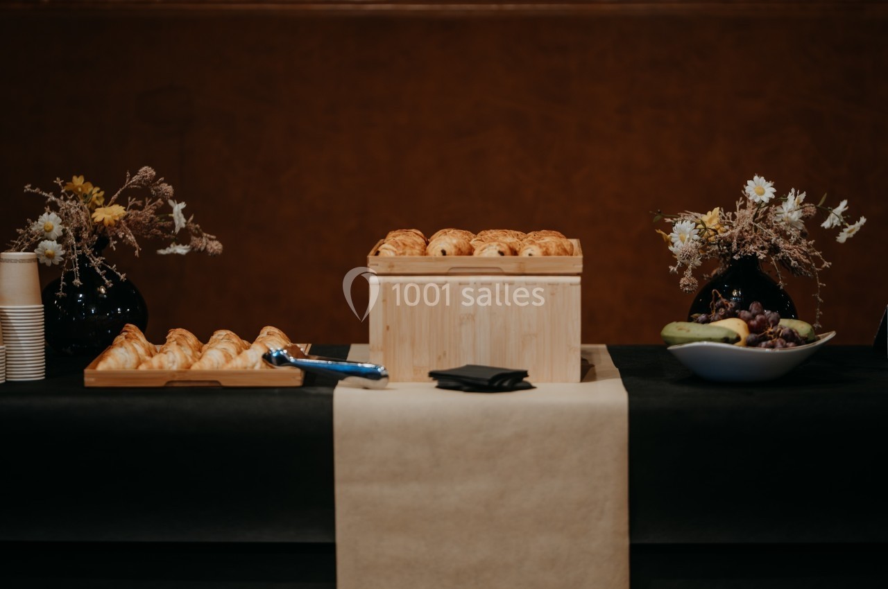 Table avec viennoiseries, fruits, fleurs séchées et gobelets, disposés pour un buffet ou une réception.