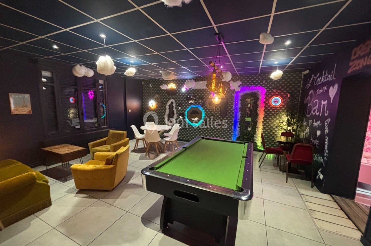 Salle de loisirs avec billard, fauteuils, table à manger et décorations lumineuses dans une ambiance moderne et colorée.