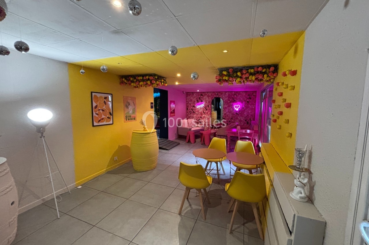 Salle lumineuse avec murs jaunes, décorations florales et néons roses, tables et chaises modernes disposées dans l'espace.