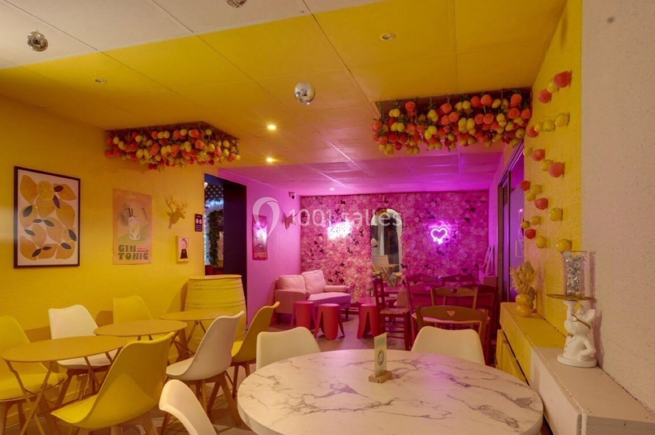 Salle colorée avec murs jaunes et roses, décorations florales, mobilier moderne et éclairage tamisé.