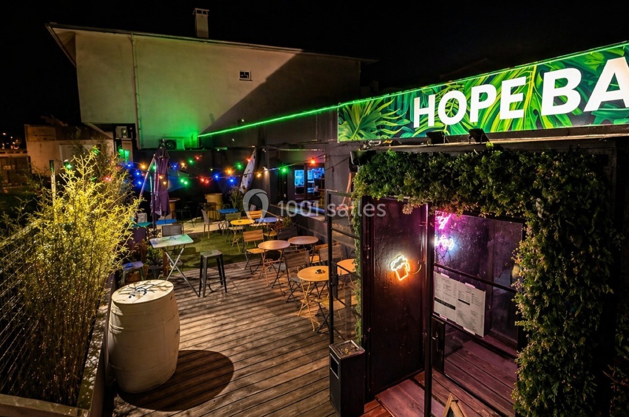 Terrasse extérieure d'un bar éclairée par des guirlandes lumineuses et des néons, ambiance nocturne.