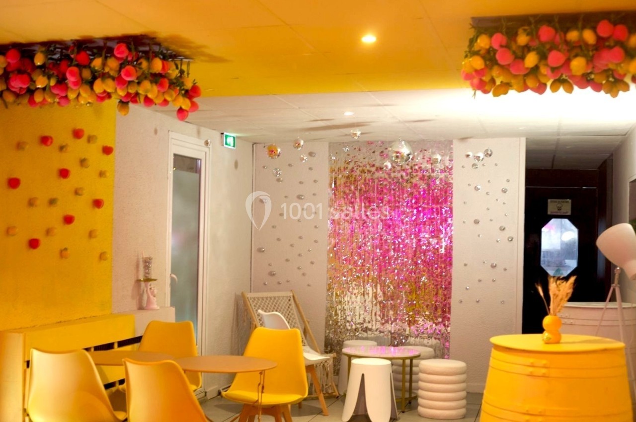 Salle lumineuse avec des murs décorés de fleurs et de guirlandes, mobilier jaune et éléments scintillants au fond.