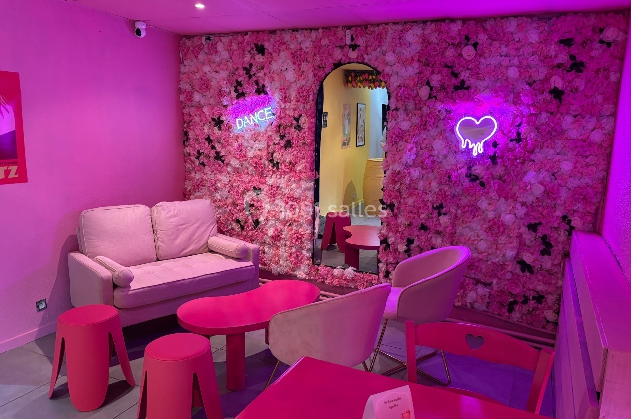 Salon décoré de tons roses avec un mur floral, des néons lumineux et des meubles assortis.