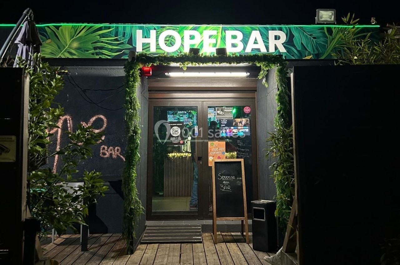 Entrée d'un bar nommé ’Hope Bar’ avec une décoration végétale et une ardoise indiquant le service du jour.