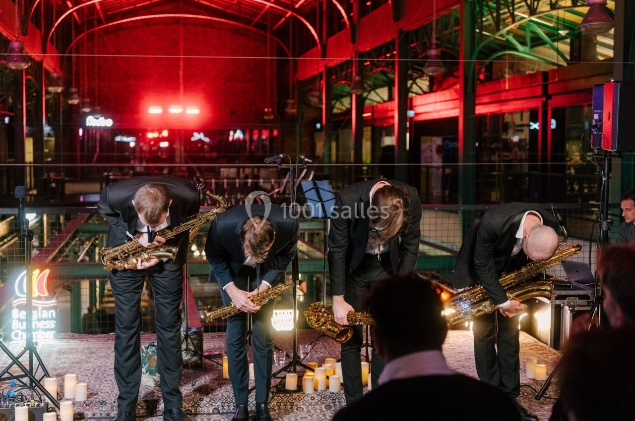 Quatre musiciens en costume saluent sur une scène éclairée, entourés de bougies, dans un espace intérieur avec une ambiance…