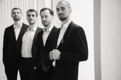 Miniature DJ Saint-Gilles (Bruxelles-Capitale) - 441 Quartet #5 Quatre hommes en costume posant debout dans un espace lumineux avec des colonnes en arrière-plan.