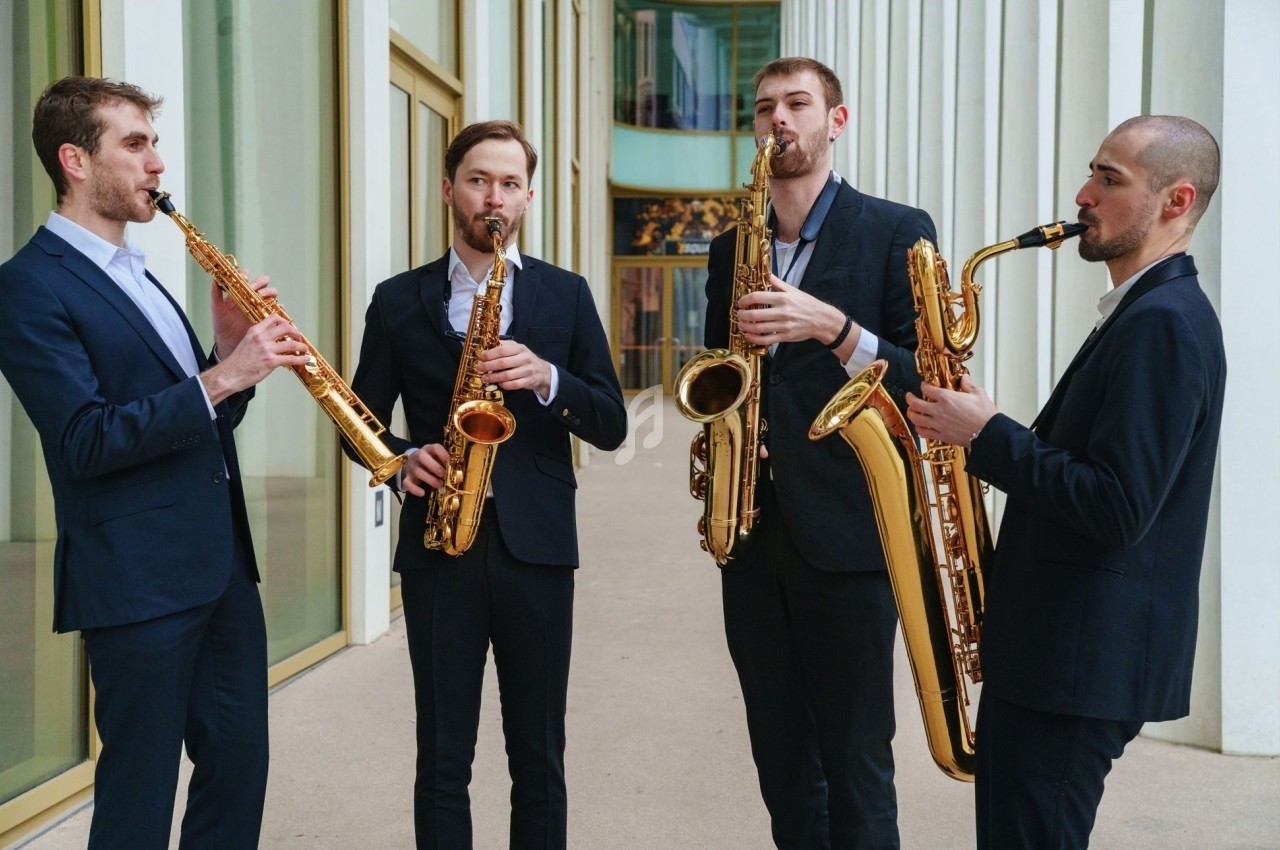 Quatuor de musiciens jouant du saxophone devant un bâtiment moderne avec des colonnes blanches.
